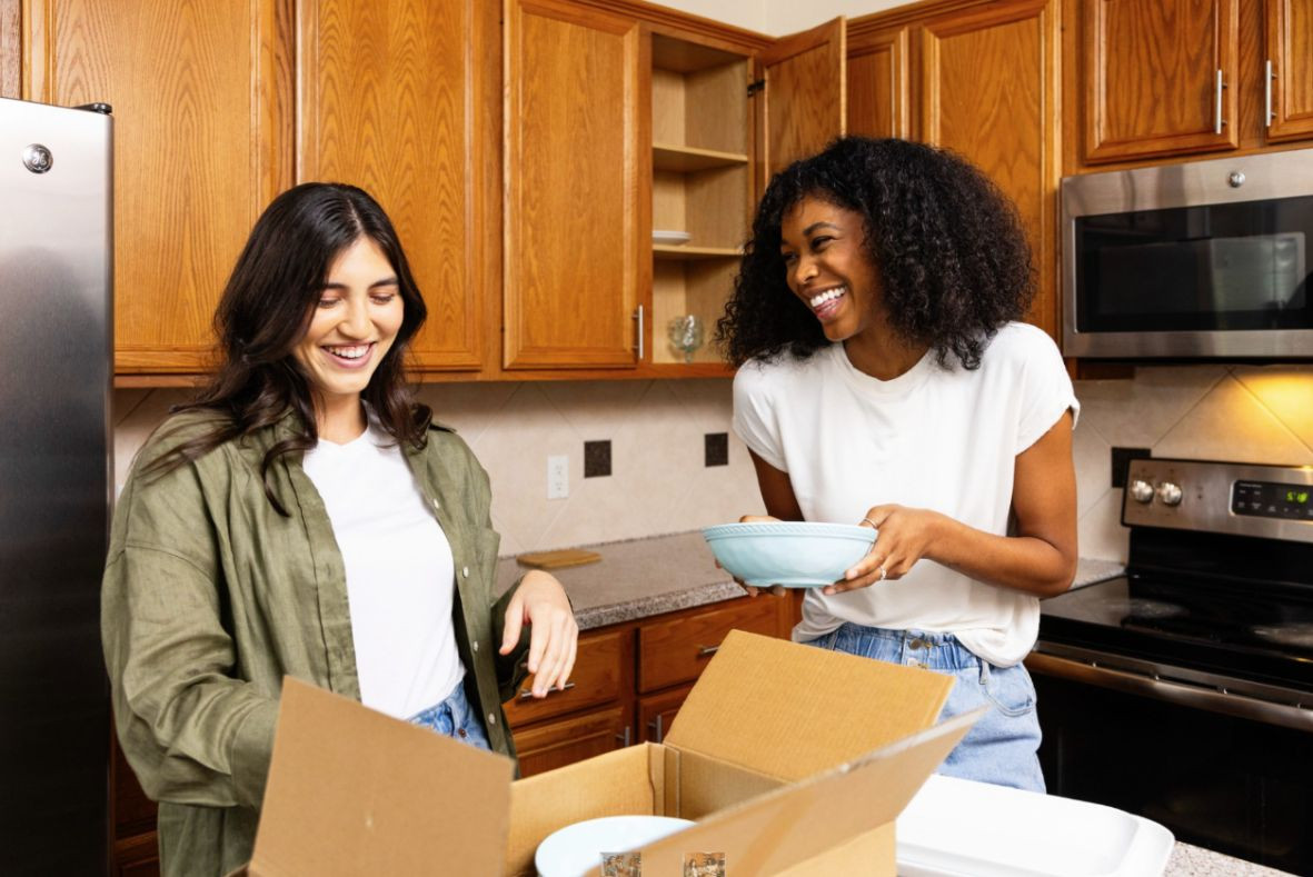 Two women smiling while unpacking kitchen items in a new apartment
